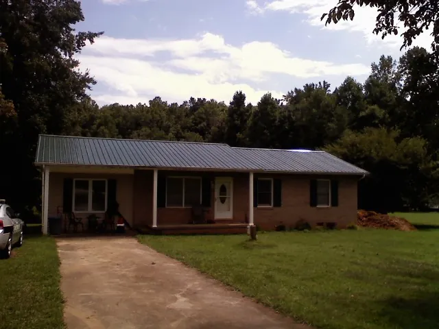 Dark green metal roof on a brick ranch with a covered porch in Bethel