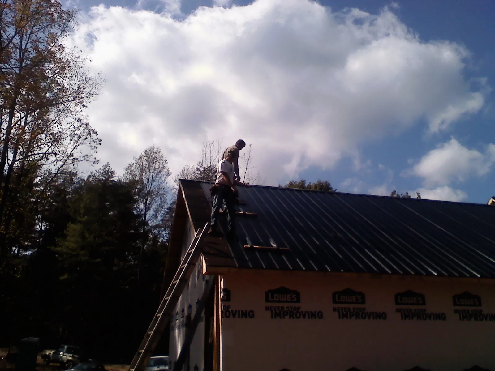 Roofer fastening dark metal panels high against a cloudy sky, from a Roof Inspection job in Bethel